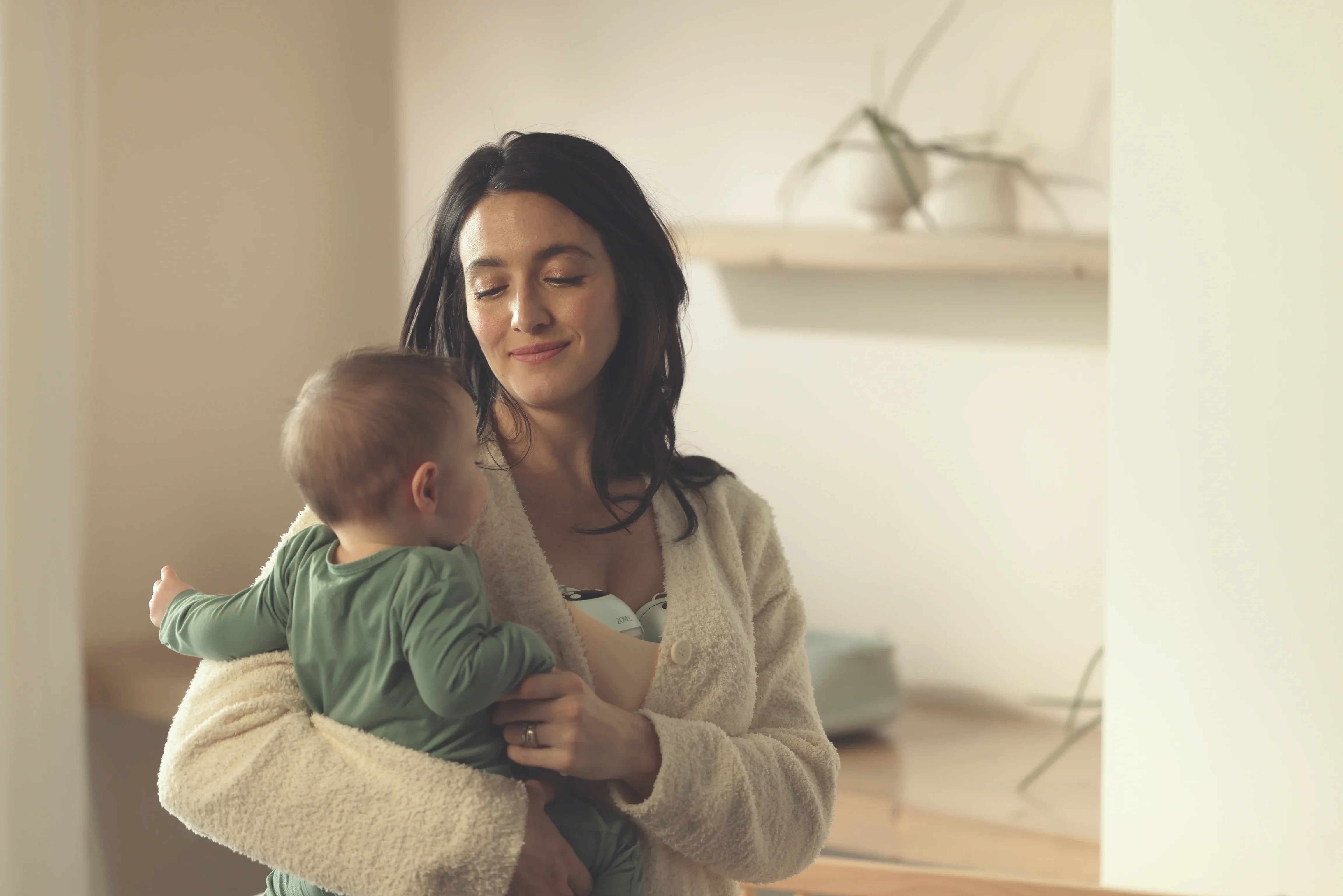 Mom holding baby while she pumps with Mother's Nature W1 Warming Wearable