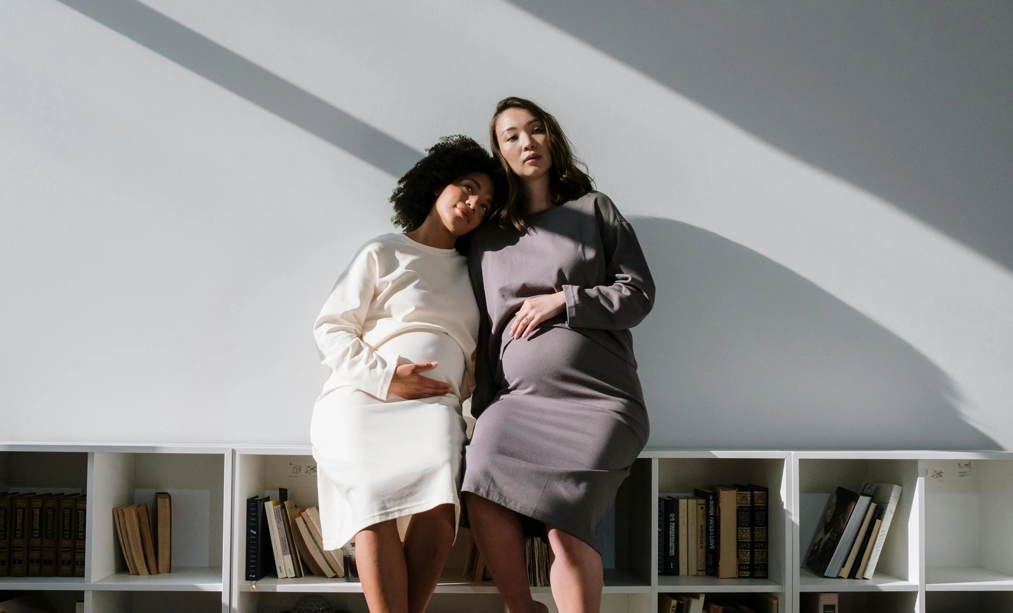 Two pregnant women holding their baby bumps posing