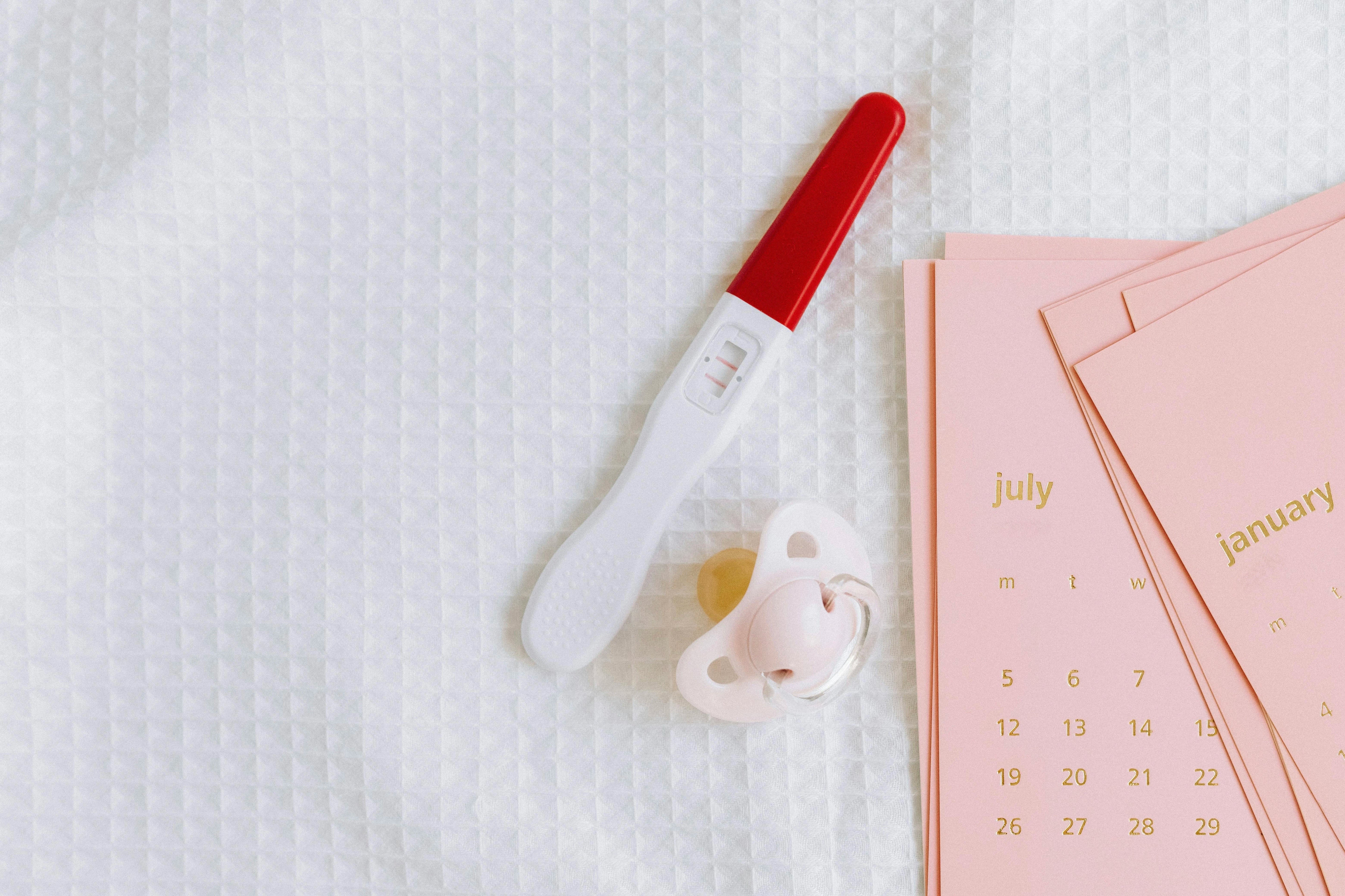 White and Red Pregnancy Test Beside a Pacifier and Pink Calendar Cards