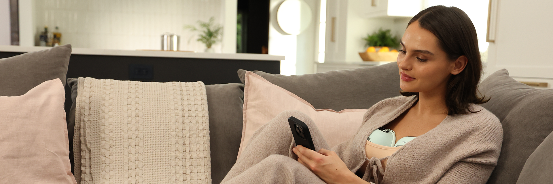 Mom using phone to search for breast pump insurance options while wearing wearable breast pumps