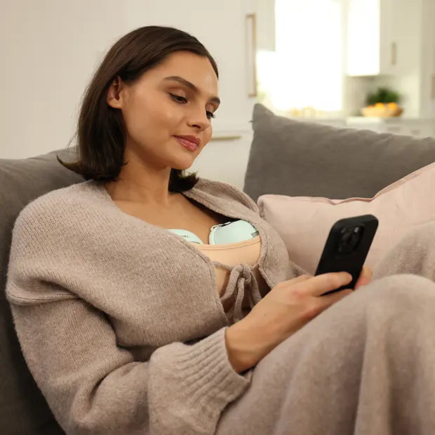 Mom using phone to search for breast pump insurance options while wearing wearable breast pumps